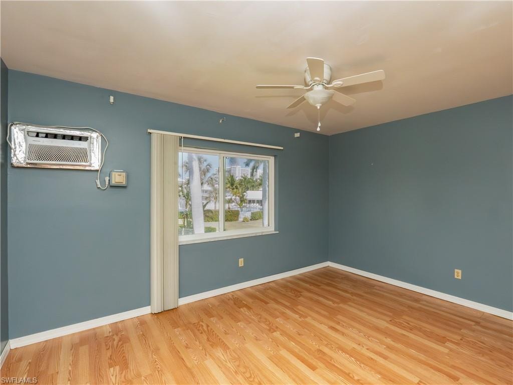Room featuring wood-finish flooring, a window with vertical blinds, a ceiling fan, and a wall-mounted air conditioning unit