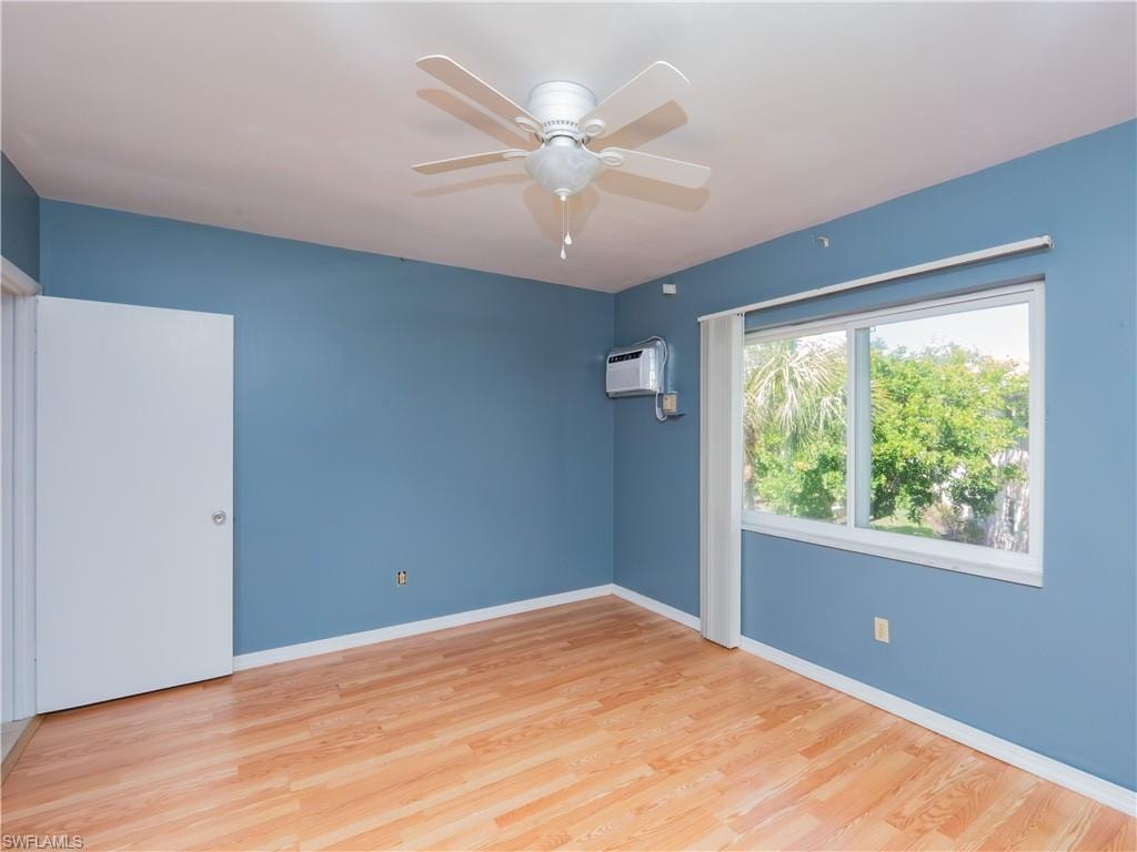 Room featuring wood-finish flooring, a ceiling fan, a window air conditioning unit, and a white-framed window with exterior tree scenery