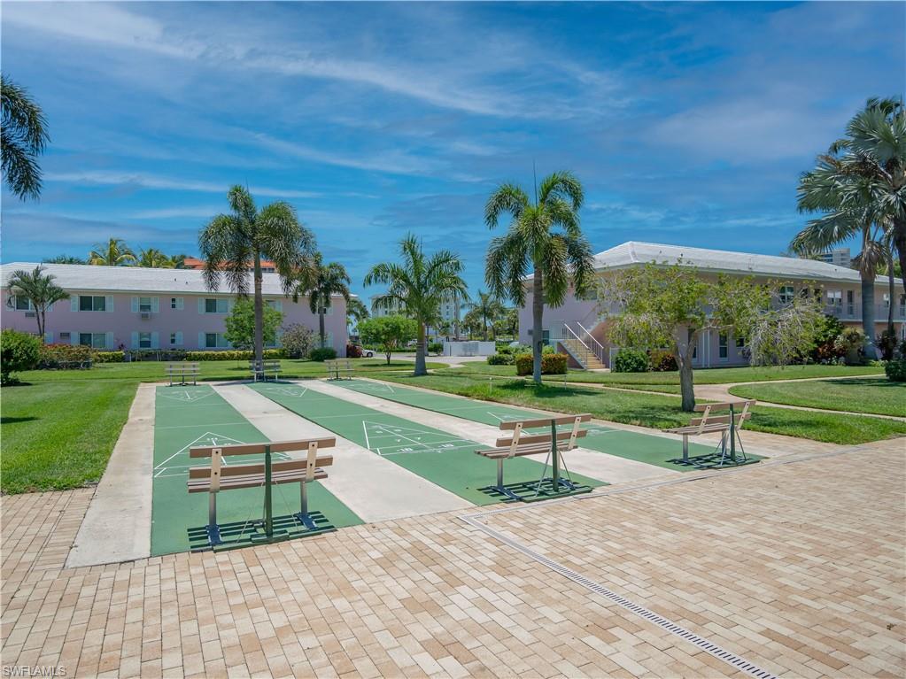Multiple outdoor shuffleboard courts with accompanying benches, surrounded by mature palm trees and manicured lawns