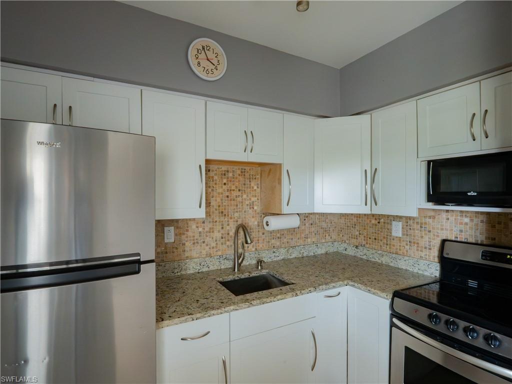 Corner kitchen with white cabinetry, stainless steel appliances, speckled countertops, and a mosaic tile backsplash