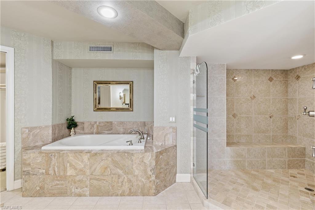 Bathroom featuring a tiled soaking tub with deck-mounted fixtures, and a glass-enclosed shower with a built-in bench
