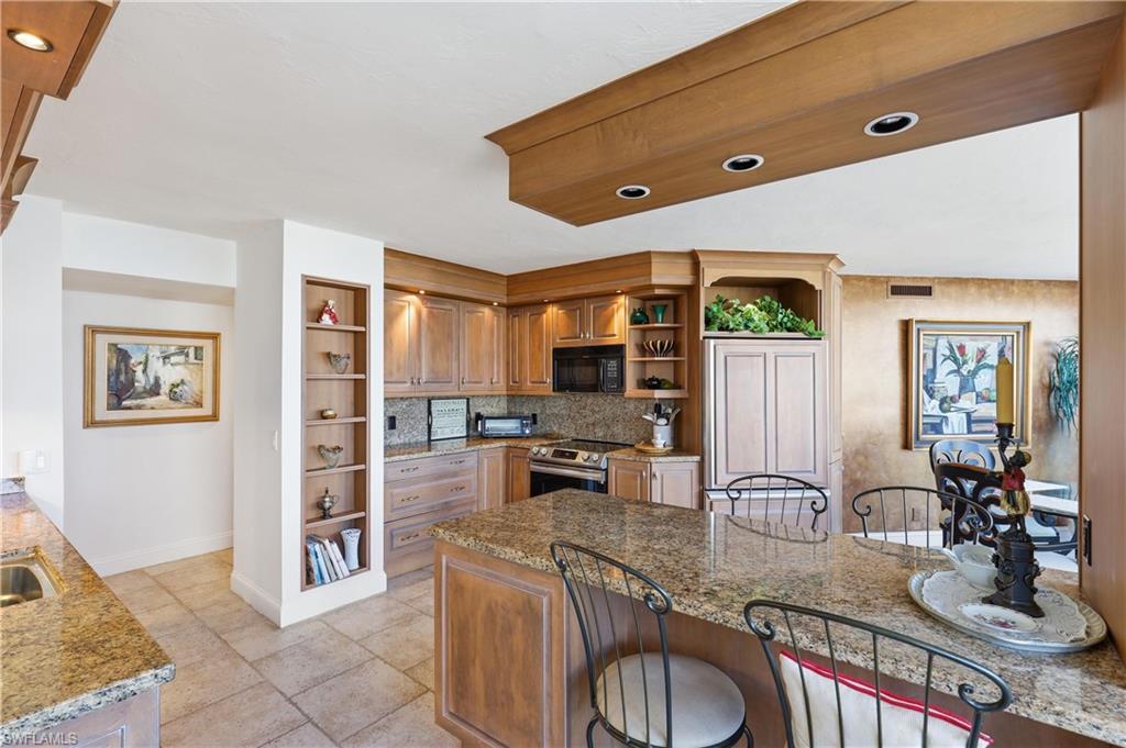 Kitchen featuring custom light wood cabinetry, stone countertops, integrated appliances, and a built-in breakfast bar