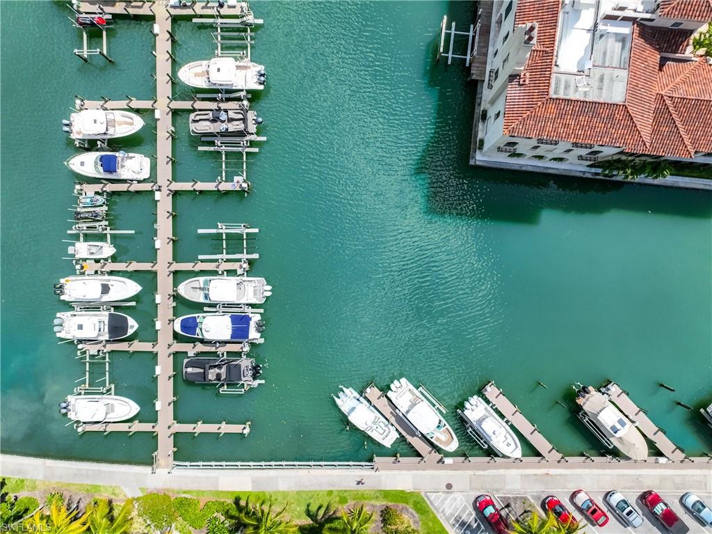 Waterfront property featuring extensive boat slips, direct water access, a multi-story building with a terracotta tile roof, and adjacent parking areas