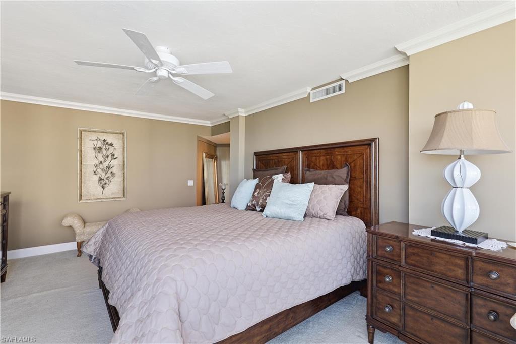 Carpeted sleeping area featuring a ceiling fan, crown molding, a dark wood-finish headboard, and warm neutral wall tones