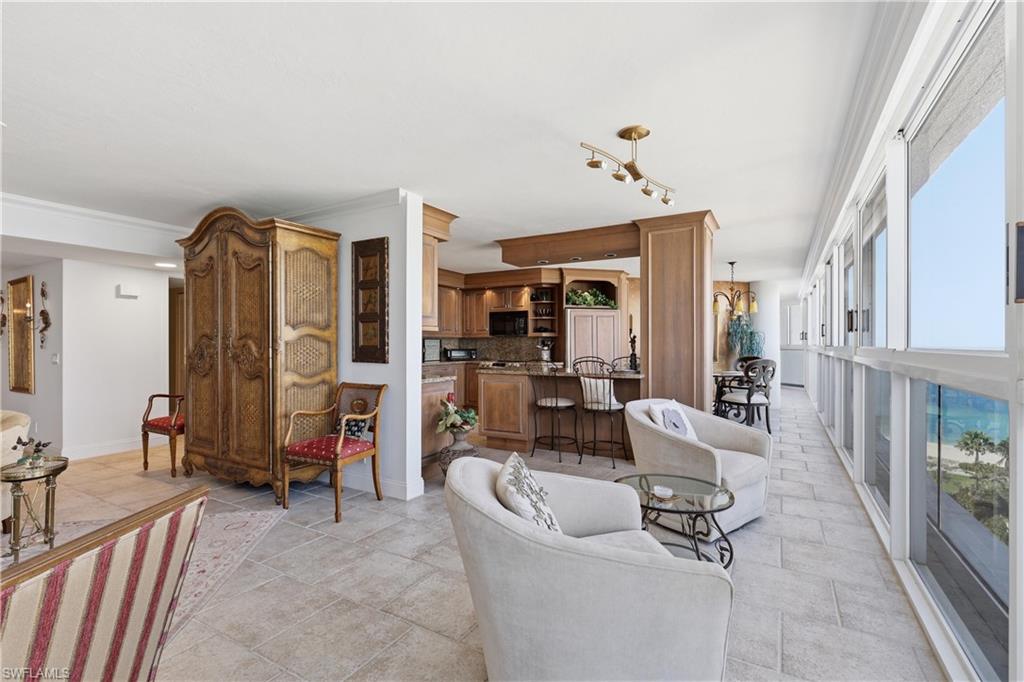 Expansive interior featuring floor-to-ceiling windows, light tile flooring, and a kitchen with wood cabinetry and granite countertops