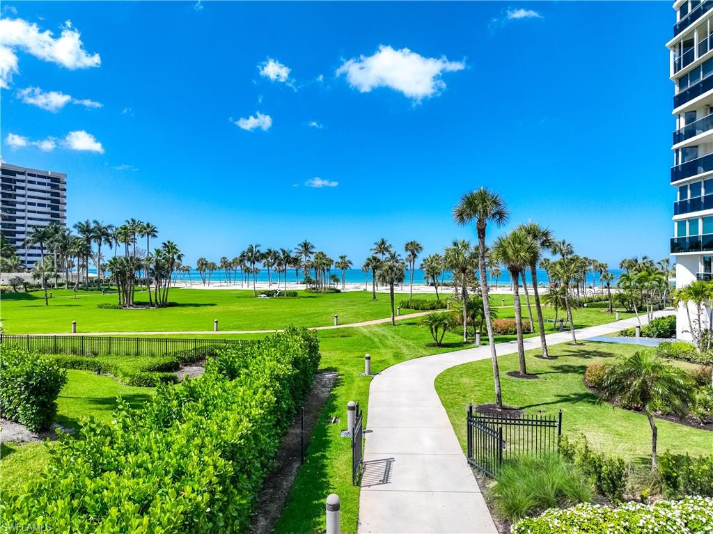 Expansive manicured lawn with mature palm trees, paved walking paths, and direct beachfront access