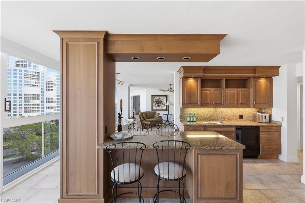 Built-in wet bar featuring granite countertops, wood cabinetry with upper and lower storage, recessed lighting, and a compact refrigerator