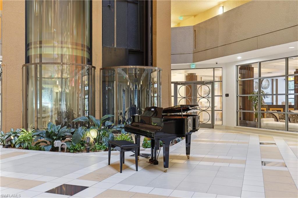 Lobby atrium featuring a grand piano, glass elevators, a planted garden area, and patterned floor tiling