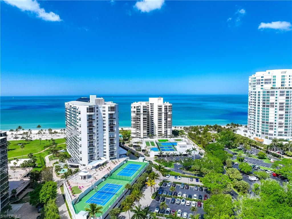 Expansive coastal community featuring multiple high-rise buildings, tennis courts, a large parking area, and manicured green spaces