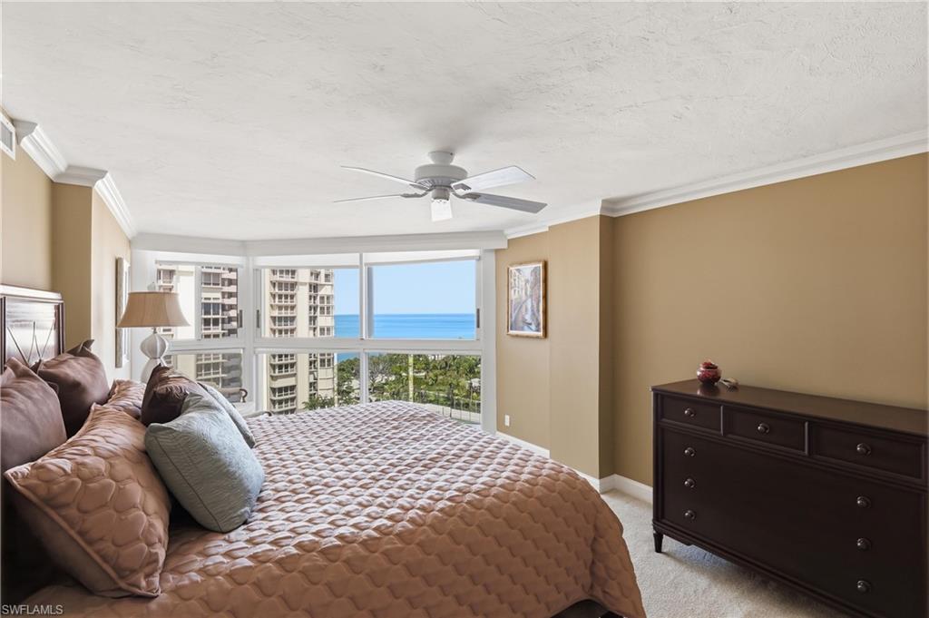 Room featuring a bay window with water and city building scenery, crown molding, a ceiling fan, and carpet flooring