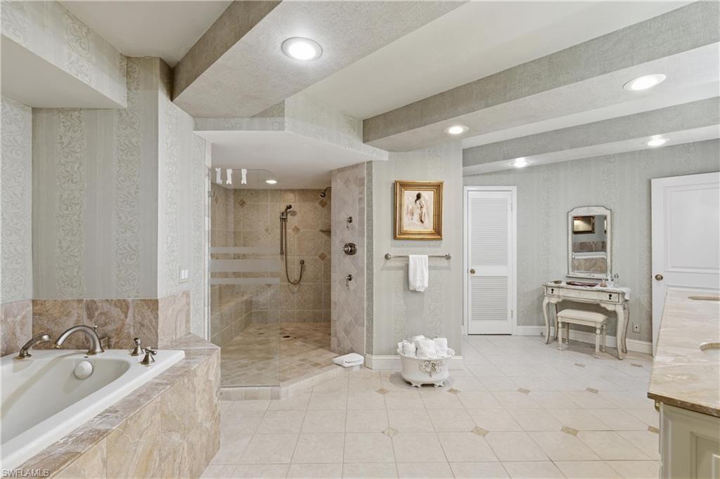 Spacious bathroom featuring a built-in tub with stone surround, a glass-enclosed shower with tiled walls, recessed lighting, and patterned wallpaper