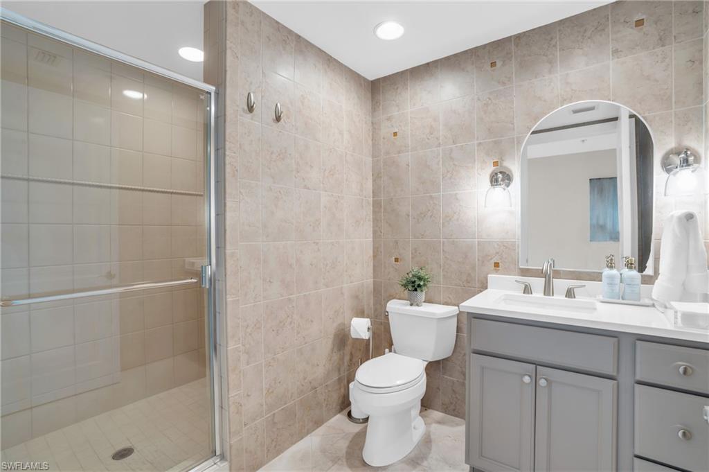 Bathroom featuring tile flooring, vanity with extensive cabinet space, an enclosed shower, tile walls, and toilet
