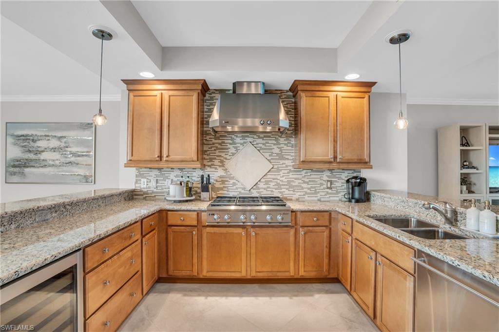 Kitchen with decorative light fixtures, wine cooler, wall chimney exhaust hood, sink, and light tile floors