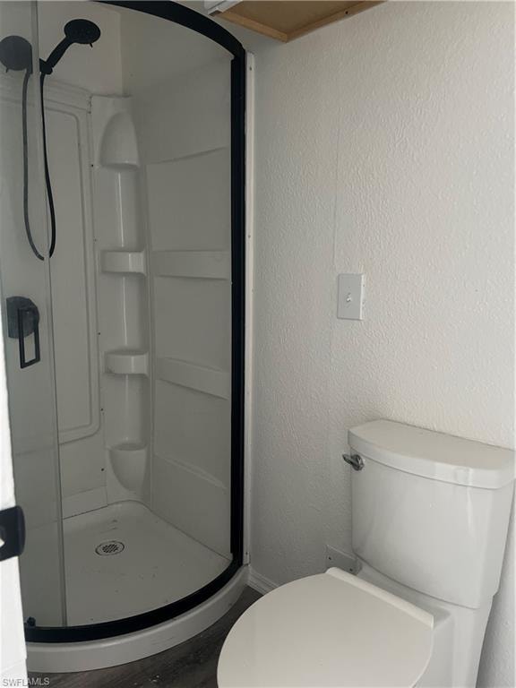 Bathroom featuring wood finished floors, a shower stall, and toilet