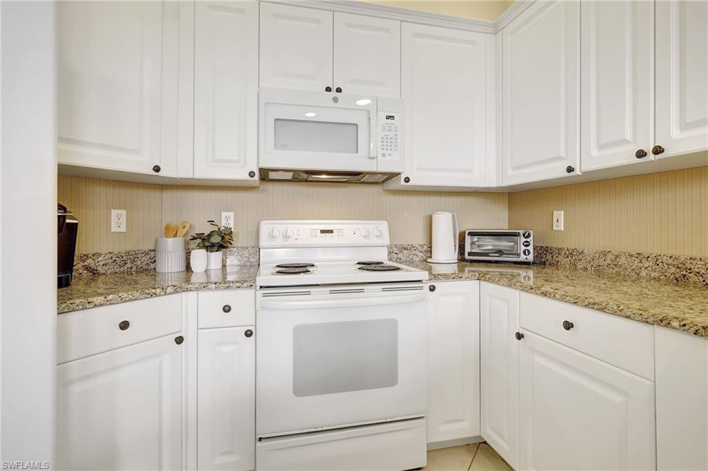 Kitchen featuring white appliances, light tile patterned floors, light stone counters, and white cabinetry