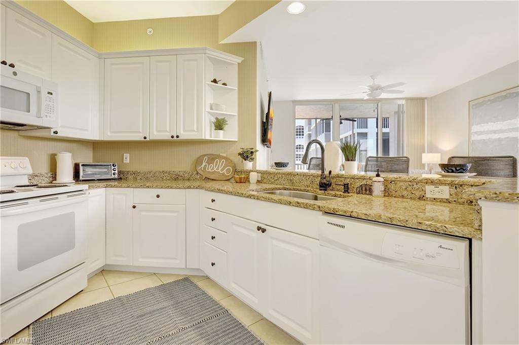 Kitchen with light stone counters, ceiling fan, white cabinetry, white appliances, and sink