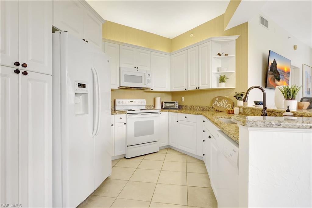 Kitchen with white cabinets, light tile patterned flooring, kitchen peninsula, and white appliances
