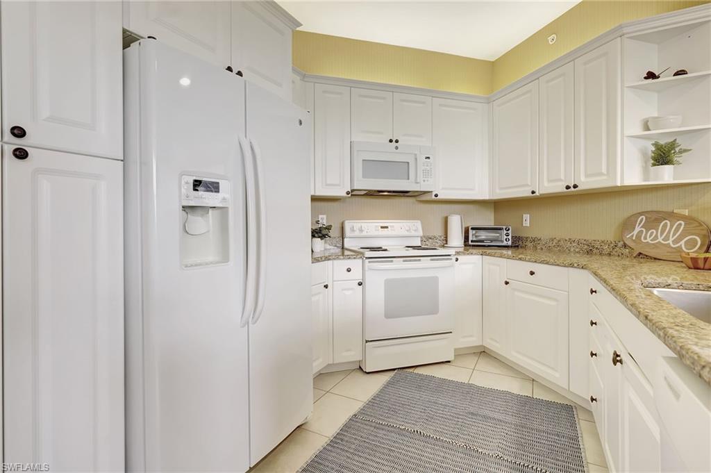 Kitchen featuring white appliances, white cabinets, light stone countertops, and light tile patterned floors