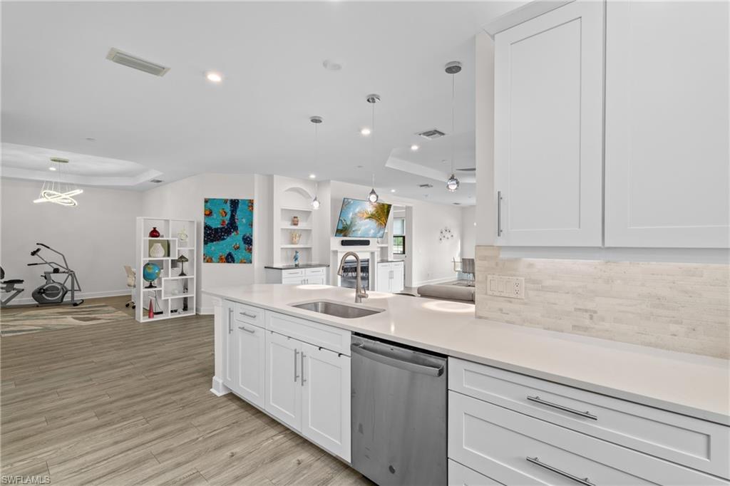 Kitchen featuring a tray ceiling, open floor plan, white cabinets, dishwasher, and recessed lighting