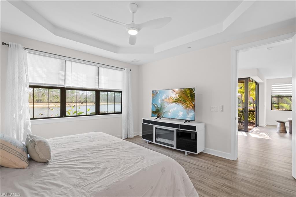 Bedroom with light wood-style flooring, ceiling fan, and a raised ceiling