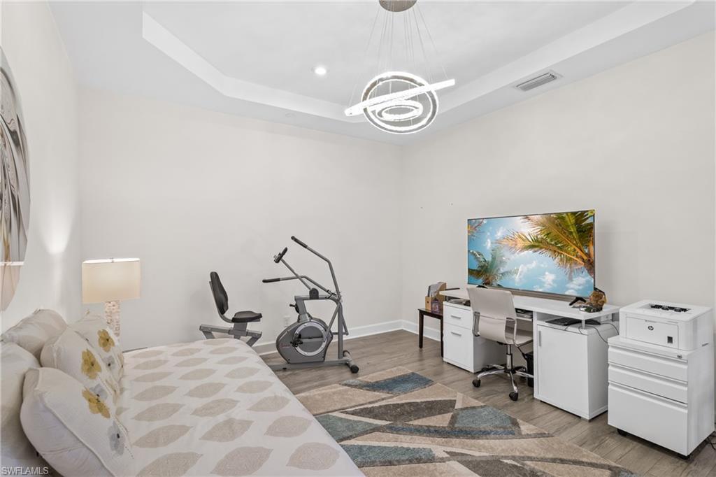 Bedroom with a tray ceiling, light wood-style flooring, a desk, and recessed lighting