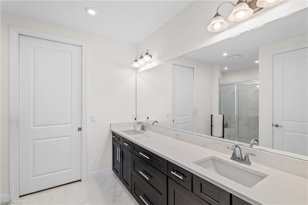 Bathroom with a marble finish shower, double vanity, light marble finish floors, and recessed lighting