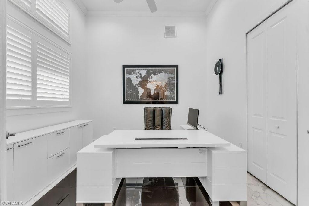 Dedicated office space featuring built-in cabinetry with modern pulls, plantation shutters, and a ceiling fan