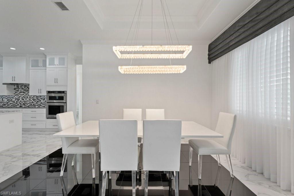 Dining area featuring a modern chandelier, white walls, and a large window with sheer white curtains and a dark valance