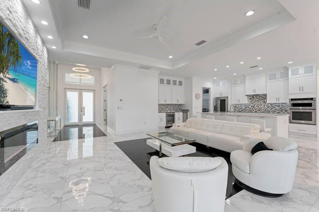 Open-concept living space featuring high ceilings with recessed lighting, marble-finish flooring, a contemporary accent wall with a built-in fireplace, and a gourmet kitchen with white cabinetry, stainless steel appliances, and a mosaic tile backsplash
