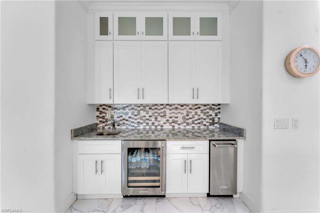 Wet bar featuring white shaker cabinetry, glass-front upper cabinets, a honeycomb tile backsplash, and a granite countertop