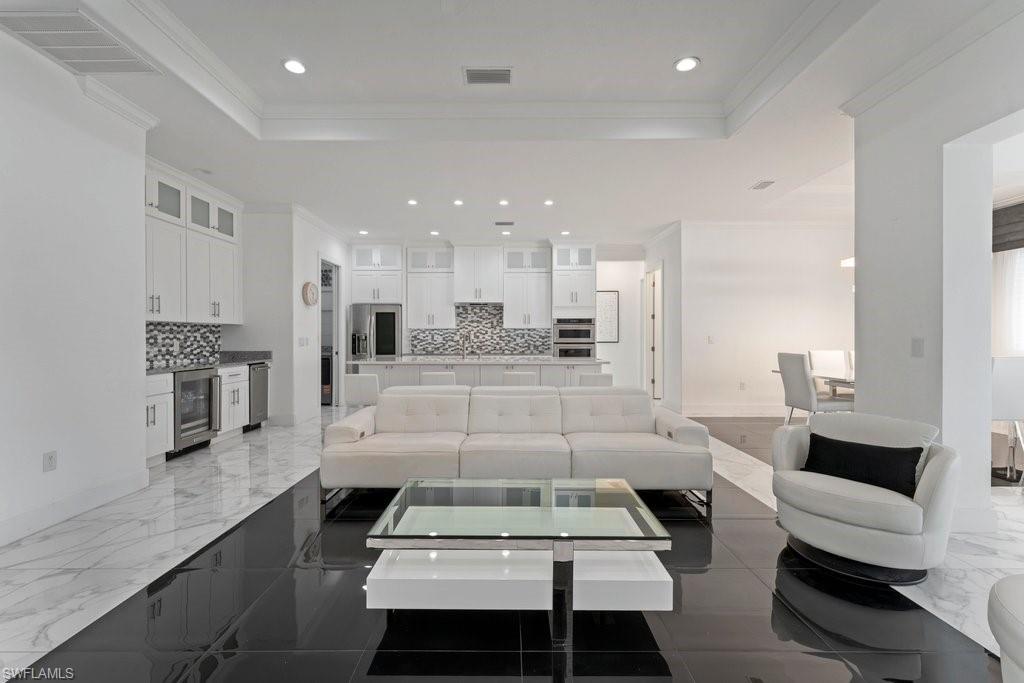 Open-concept living area featuring a large kitchen with white cabinetry, stainless steel appliances, and a mosaic tile backsplash