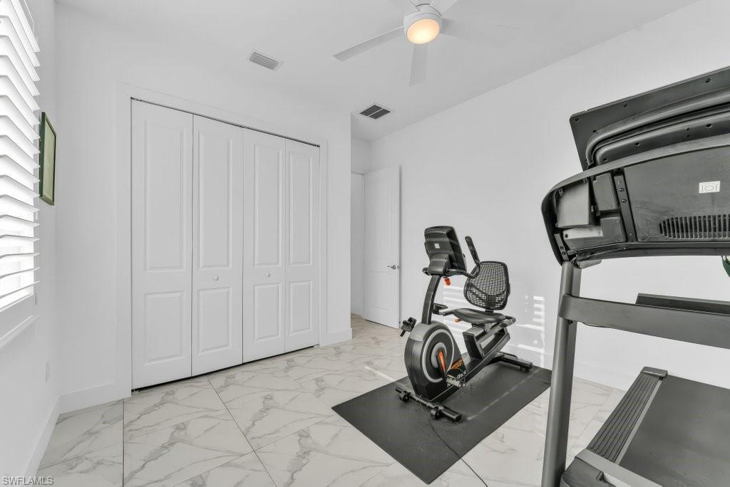 Room featuring large format marble-look floor tiles, a window with white louvered shutters, bi-fold closet doors, and an overhead ceiling fan with integrated lighting
