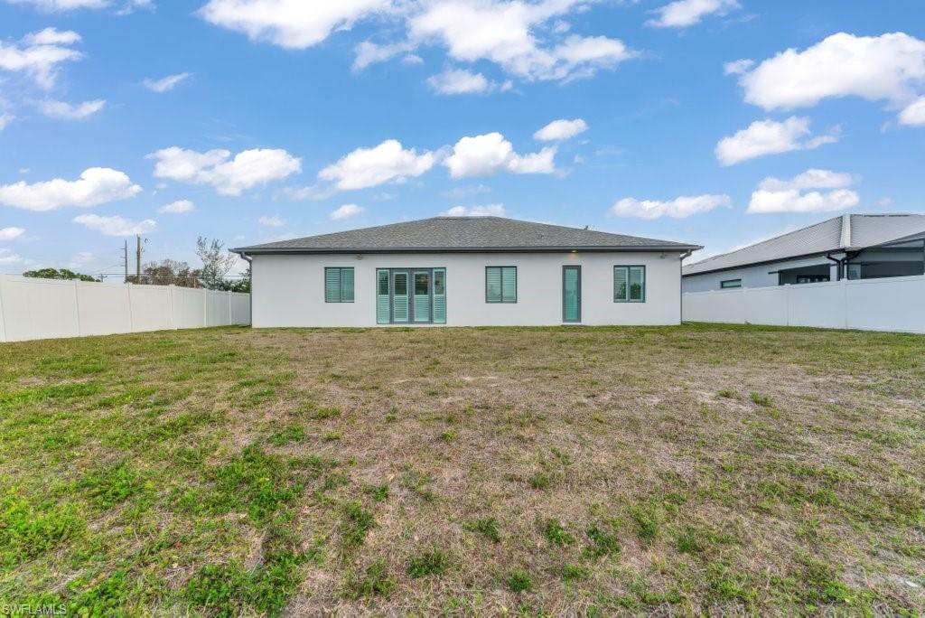 Expansive backyard featuring a new construction stucco exterior, multiple windows, and a set of glass doors