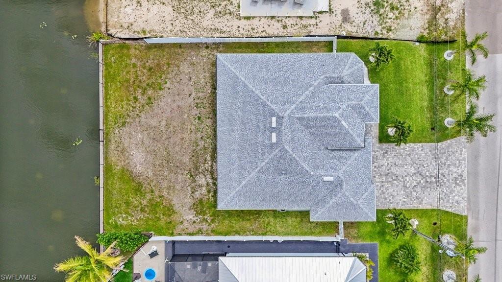Waterfront property featuring a gray shingle roof, green lawn, a concrete driveway, and palm trees
