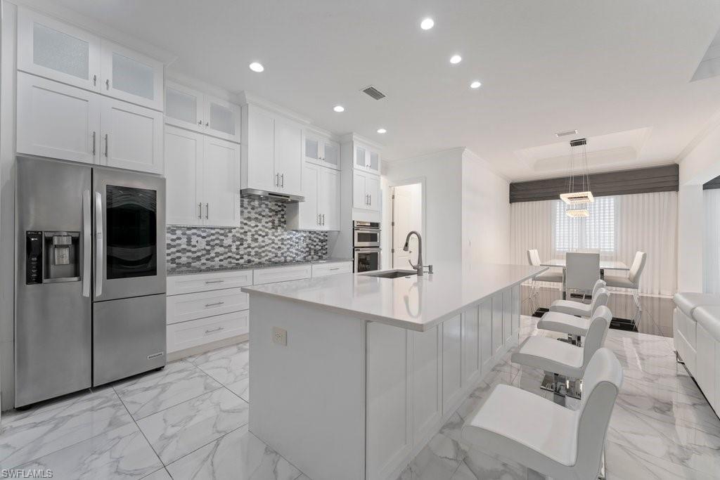 Modern kitchen featuring white cabinetry, a large center island with seating, stainless steel appliances, and a mosaic tile backsplash