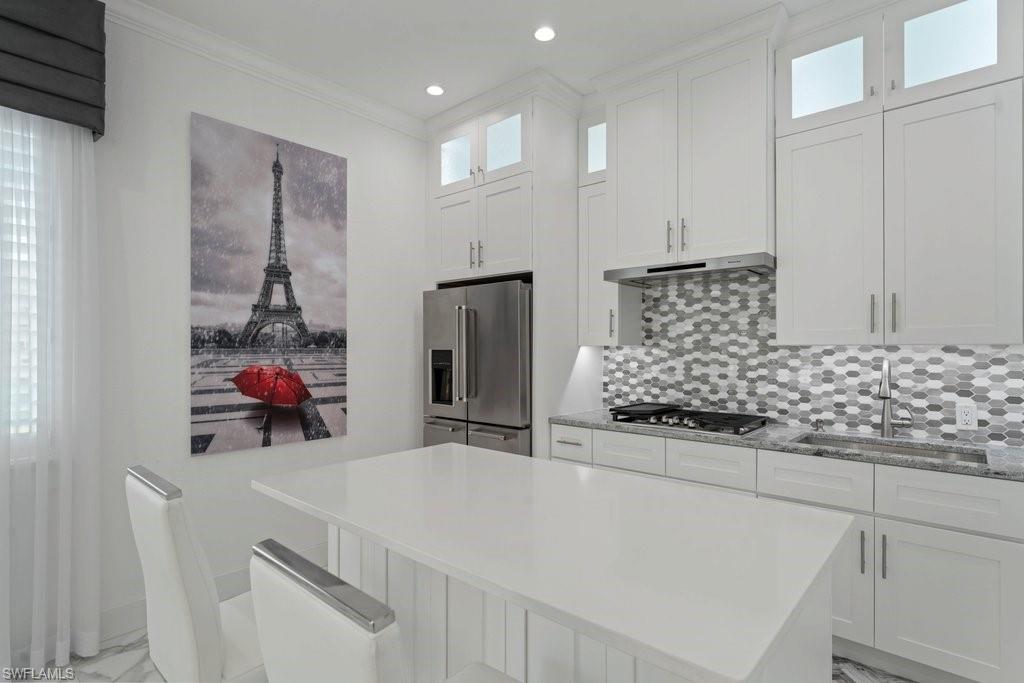 Kitchen featuring a large central island, white cabinetry with upper transom windows, stainless steel appliances, mosaic tile backsplash, and stone countertops