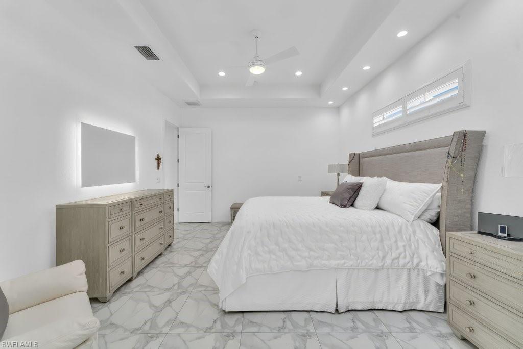 Spacious bedroom featuring contemporary marble-look tile flooring, a tray ceiling with recessed lighting, and a modern ceiling fan