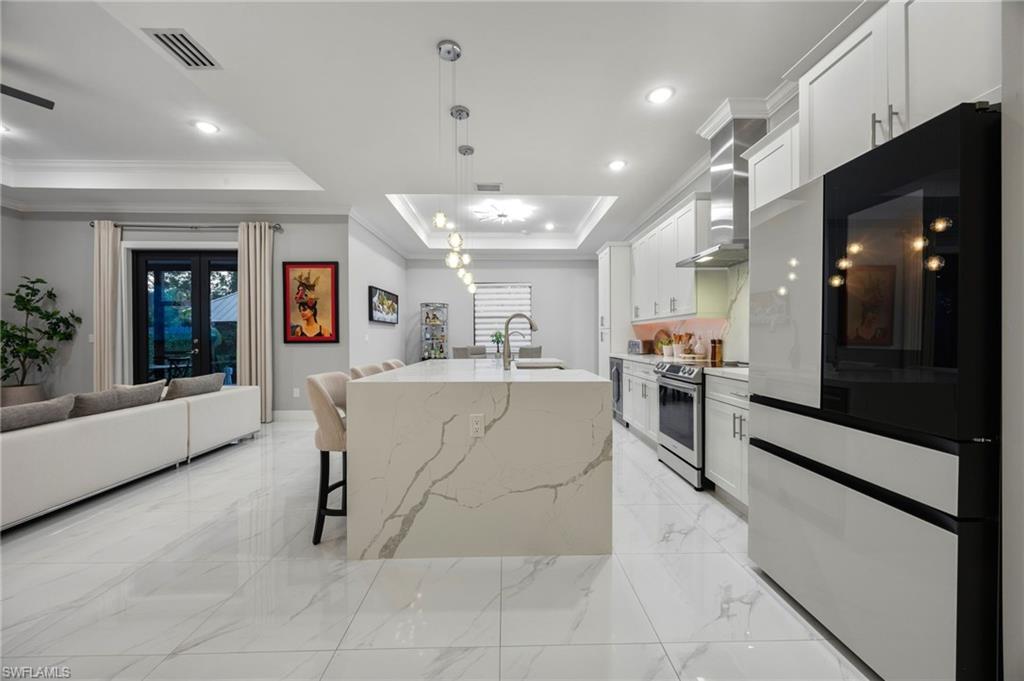 Contemporary kitchen featuring a waterfall-edge island, white shaker-style cabinetry, stainless steel appliances, and large format tile flooring
