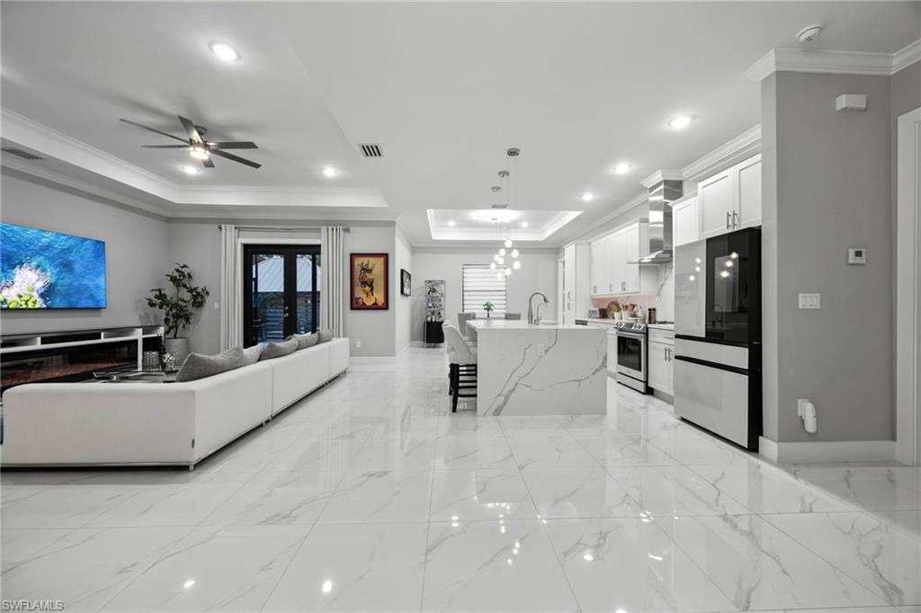 Open-concept living space featuring high ceilings with recessed lighting, crown molding, and large format marble-look tile flooring