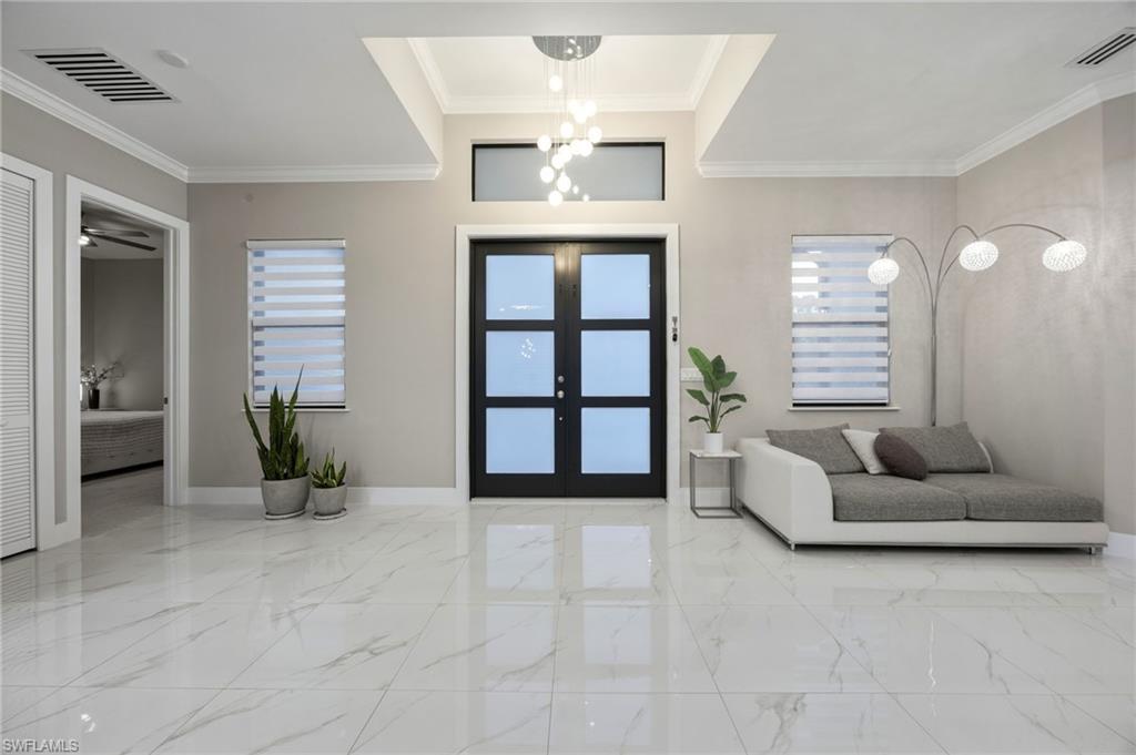 Entry foyer featuring polished tile flooring, a contemporary chandelier, crown molding, and a transom window above the entry door