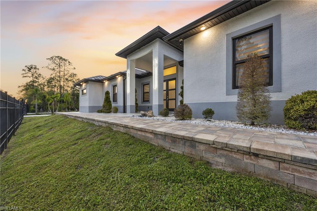Contemporary exterior featuring a stucco finish, dark framed windows, and a paved walkway with a stone retaining wall