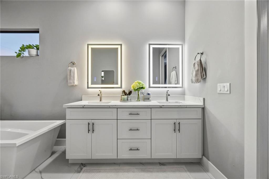 Dual vanity in primary bathroom with white cabinetry, integrated sinks, and polished chrome fixtures