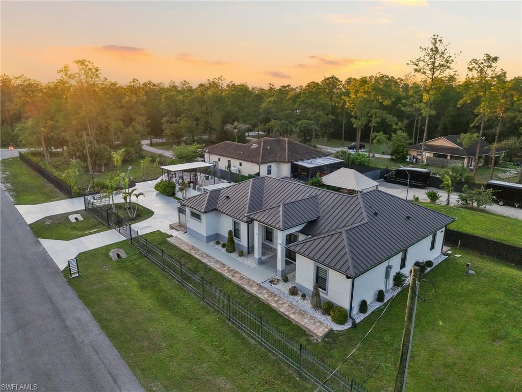Contemporary residence featuring a dark metal standing seam roof, white stucco exterior, and a paved circular driveway