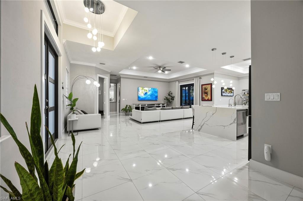 Spacious interior featuring large format marble-look tile flooring, a contemporary kitchen island with a waterfall countertop, and a tray ceiling with recessed lighting