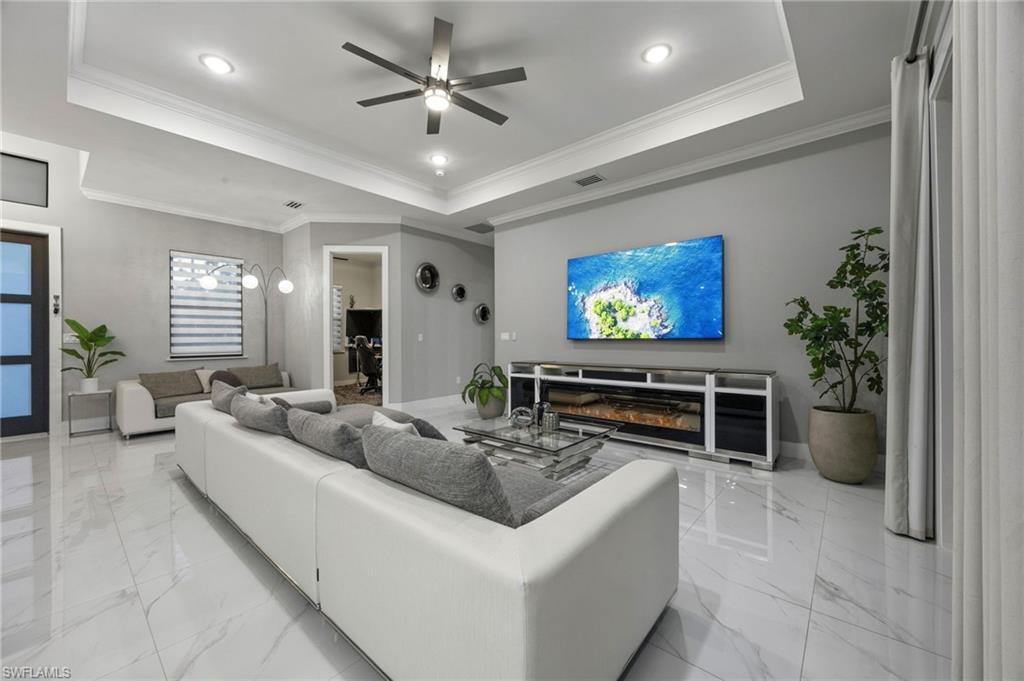 Spacious living area featuring polished tile flooring, a tray ceiling with recessed lighting, and a contemporary ceiling fan