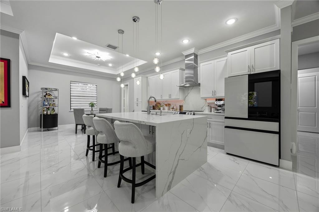 Gourmet kitchen featuring a waterfall island with integrated seating, white shaker cabinetry, stainless steel appliances, and a tray ceiling with recessed lighting