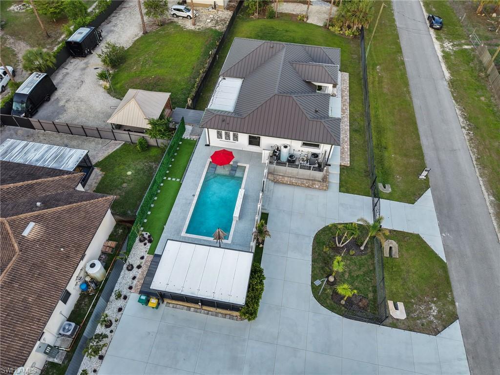 Contemporary residence featuring a rectangular pool with surrounding patio, a concrete driveway, a dedicated covered patio area, and a secondary structure with a gabled roof