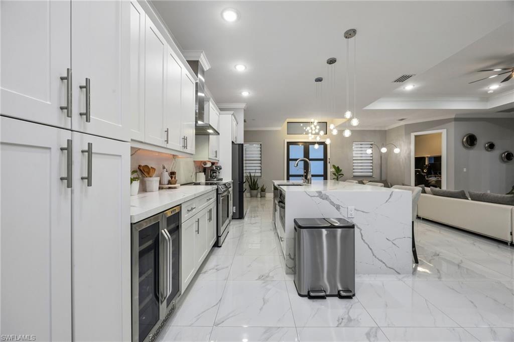 Gourmet kitchen featuring white shaker cabinetry, an oversized waterfall island with a single basin sink, and integrated beverage cooler
