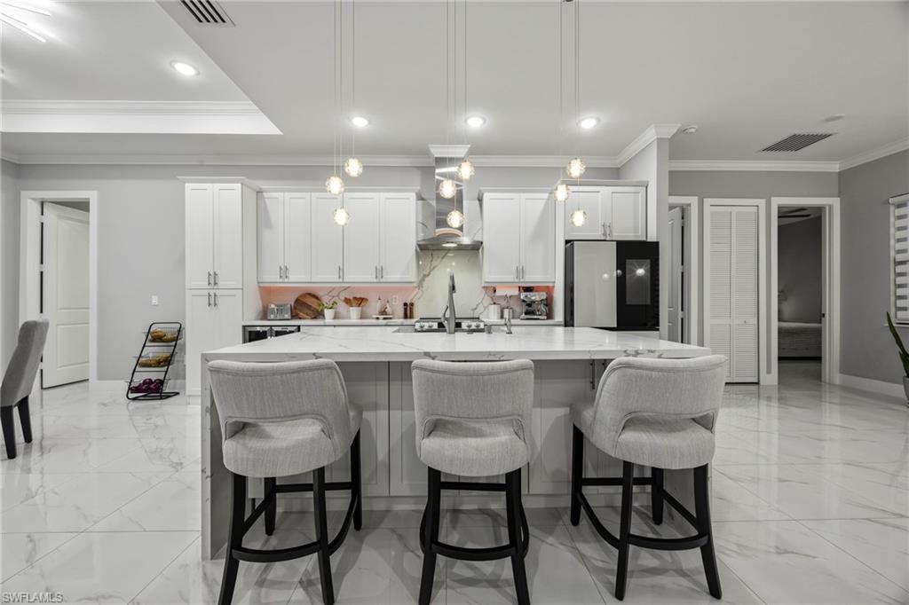 Modern kitchen featuring a central island with a waterfall countertop, pendant lighting, white cabinetry, integrated range hood, and large format tile flooring