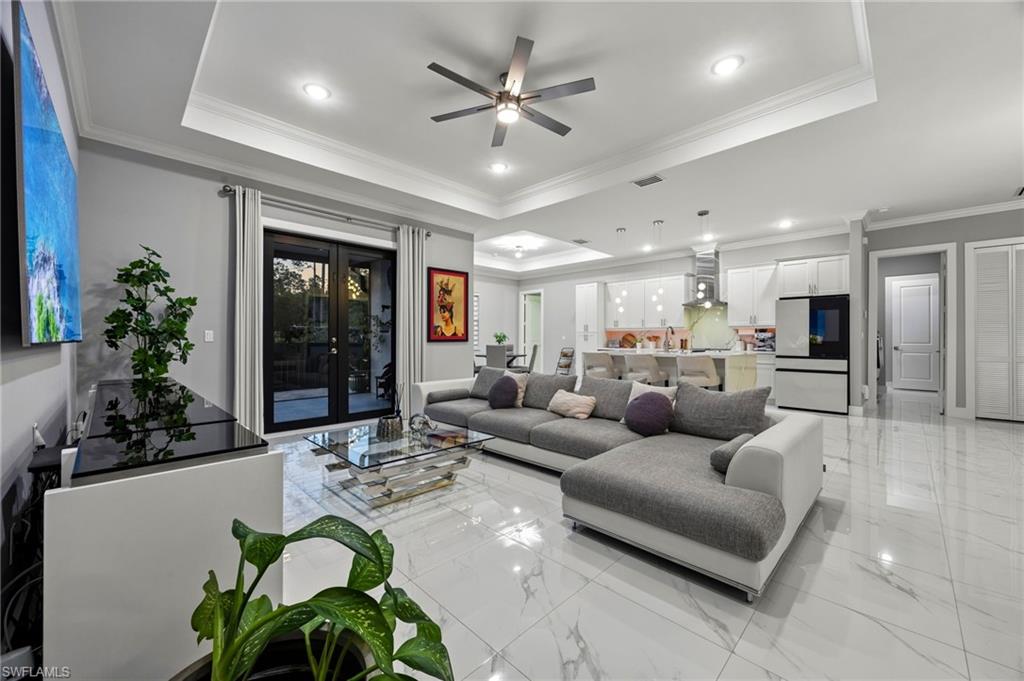 Spacious living area featuring polished tile flooring, a tray ceiling with recessed lighting, and a ceiling fan